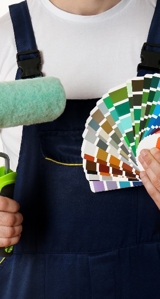 Choix de Couleurs Peinture : Outils du Peintre Peintre professionnel en salopette marine et t-shirt blanc tenant un rouleau à peindre vert d'eau et une palette d'échantillons de couleurs.