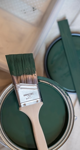 Pinceau et peinture vert forêt pour rénovation Pinceau de peinture 2 pouces (50.8mm) chargé de peinture vert forêt, reposant sur une boîte de peinture ouverte.